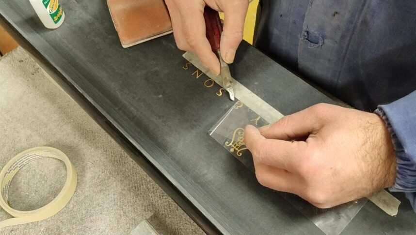 Le mani di un restauratore applicano in foglia d'oro la scritta Steinway & Sons sul frontalino di un pianoforte
